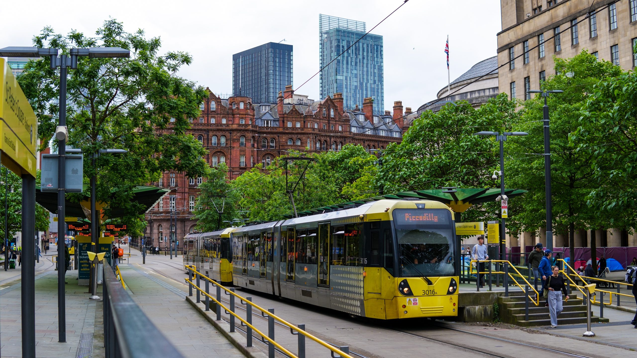 Yellow Manchester tram at a stop in St Peter's Square with Betham Tower in the background.