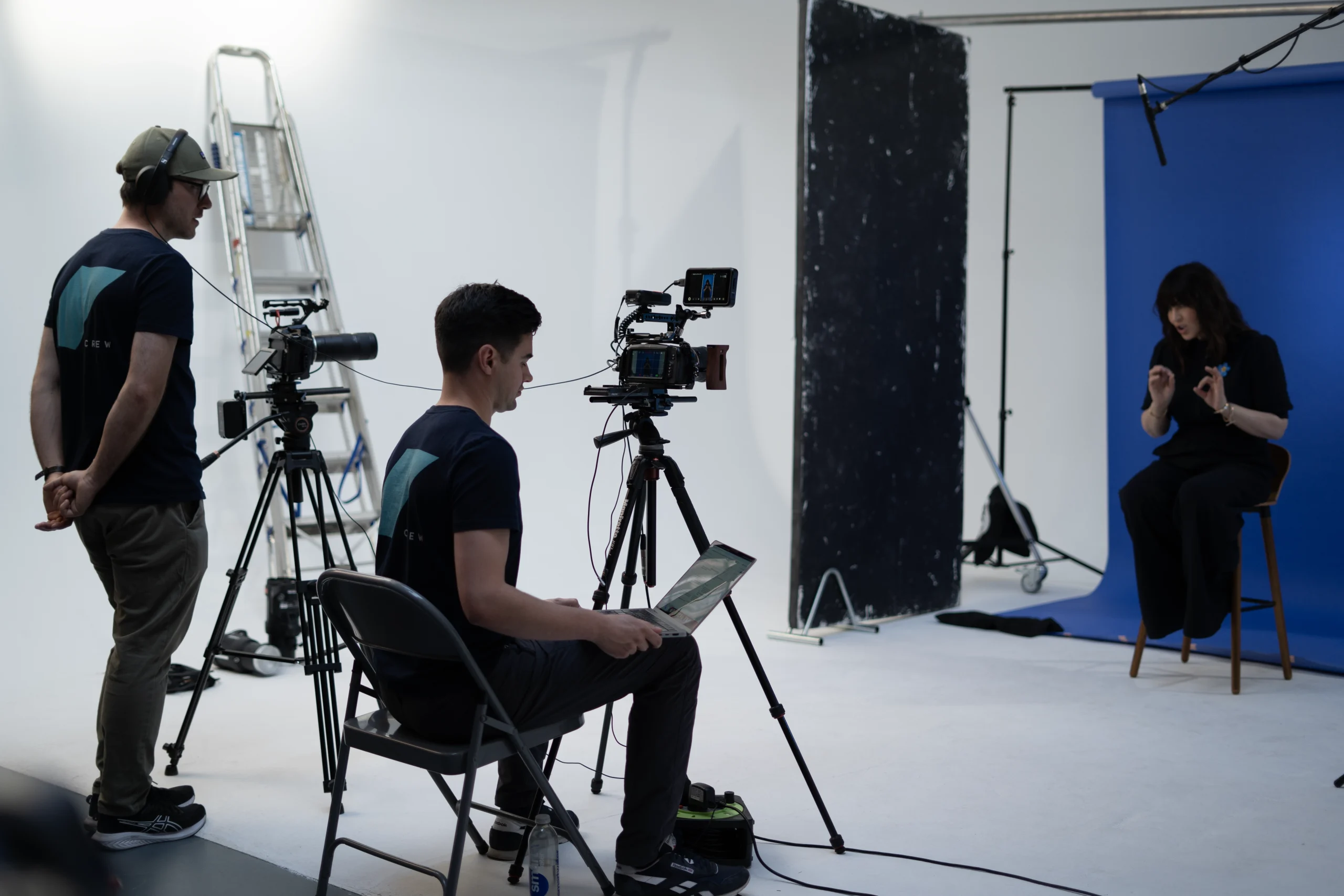 An explainer video production set featuring the production crew from Glacé Media as well as an individual on camera sat in front of a blue backdrop in a video studio.